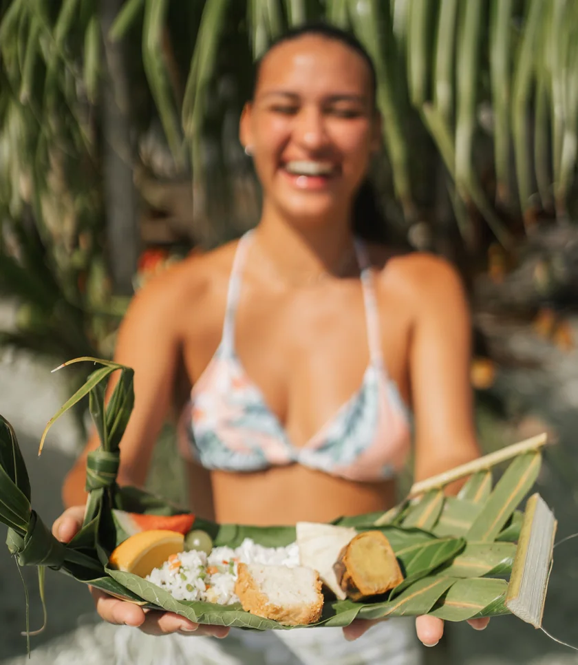 Smiling Polynesian hostess presenting a lunch served on palm leaves in Bora Bora